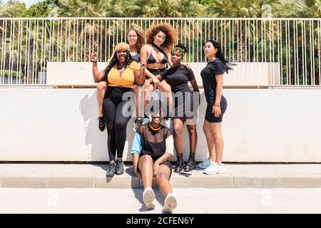 Groupe de jeunes amies multiraciales se réunissant sur le trottoir et regarder l'appareil photo Banque D'Images