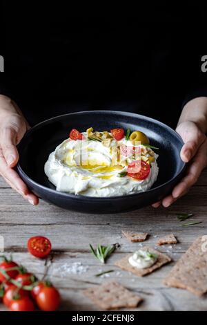 Craquelins croquants et romarin placés sur une table en bois près de la serviette et assiette de yaourt de labneh avec tomates et olives Banque D'Images