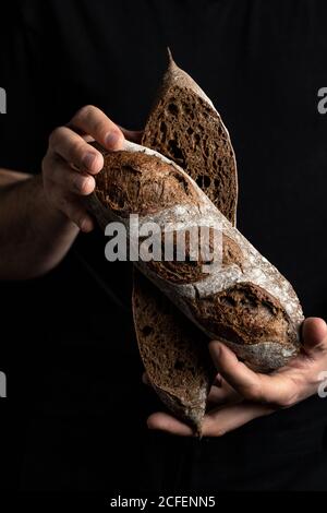 Crop mâle boulanger dans le tablier tenant coupé en demi-pain de pain frais et sain artisanal Banque D'Images