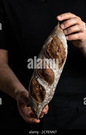 Crop mâle boulanger dans un tablier tenant le pain frais et sain artisan Banque D'Images