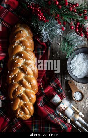 Vue de dessus d'une table en bois avec pain tressé traditionnel coupé Et couteau placé sur la nappe de Noël à carreaux avec des objets décoratifs Banque D'Images