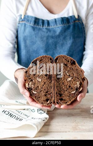 Mains de la femme en tablier tenant le pain de seigle avec les raisins secs et les noix Banque D'Images