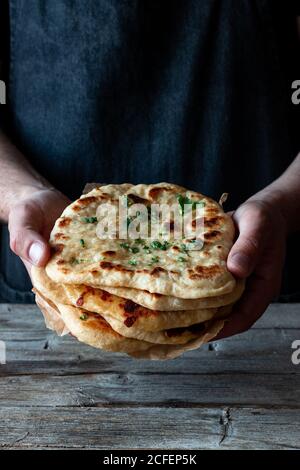 homme méconnaissable tenant une pile de pain plat naan frais sur du bois table dans la cuisine rustique Banque D'Images