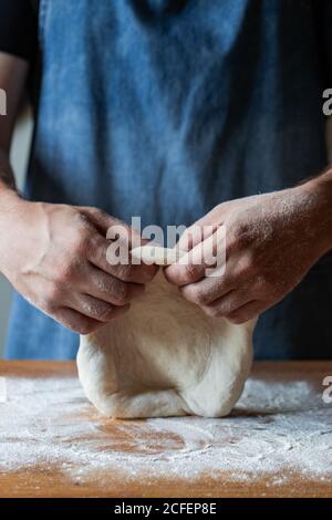 un homme méconnu en tablier aplatit la pâte molle sur la table avec farine tout en cuisant de la pizza Banque D'Images