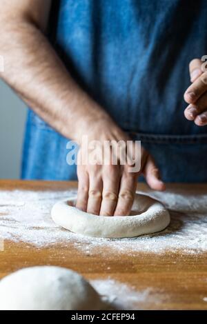 un homme méconnu en tablier aplatit la pâte molle sur la table avec farine tout en cuisant de la pizza Banque D'Images