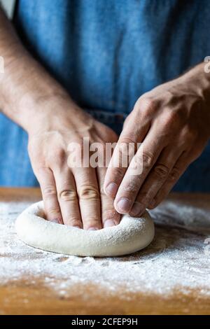 un homme méconnu en tablier aplatit la pâte molle sur la table avec farine tout en cuisant de la pizza Banque D'Images