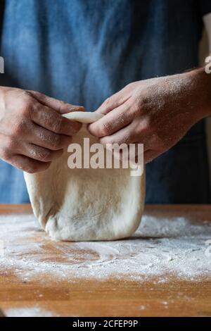 un homme méconnu en tablier aplatit la pâte molle sur la table avec farine tout en cuisant de la pizza Banque D'Images