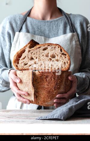 Mains de la femme dans le tablier de cuisine tenant les deux mains coupant du pain fait maison Banque D'Images