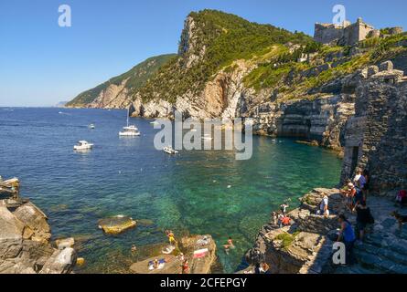 Vue sur la baie de la grotte du Seigneur Byron avec les personnes qui nagent et bronzer sur les rochers et le château de Doria au sommet de la falaise, Porto Venere Banque D'Images