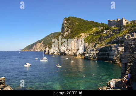 Vue sur la baie de la grotte du Seigneur Byron avec les personnes qui nagent et bronzer sur les rochers et le château de Doria au sommet de la falaise, Porto Venere Banque D'Images