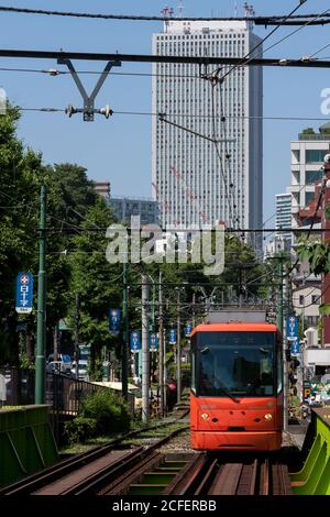 Un tramway ou une voiture de rue sur la ligne Toden Arakawa, connue sous le nom de tramway Tokyo Sakura, devant un grand immeuble de bureaux moderne à Tokyo, au Japon. Banque D'Images