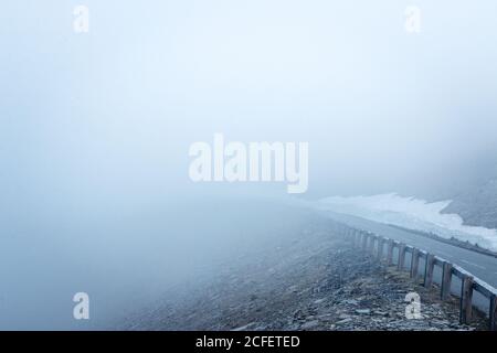 Route asphaltée étroite sur une pente de montagne à travers une épaisse brume dans la nature Banque D'Images