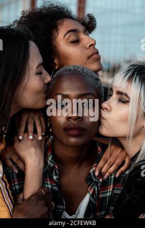 Portrait d'une jeune femme noire à poil court regardant un appareil photo avec un visage sérieux tandis que des amies de soutien avec des câlins et des baisers Banque D'Images