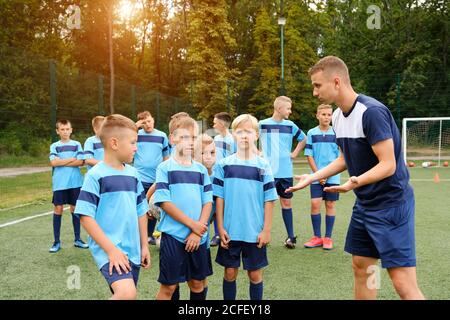 Les enfants en uniforme de soccer écoutent les explications de l'entraîneur pendant l'entraînement. Banque D'Images