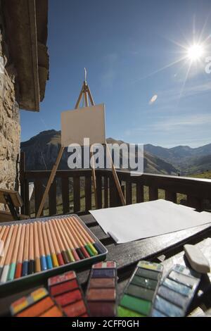 Jeu de crayons colorés et divers outils de peinture placés sur table en bois près du chevalet avec toile sur la terrasse ensoleillée de Ancienne maison en pierre en Espagne Banque D'Images