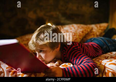 Enfant rêveur dans une tenue décontractée allongé sur un lit confortable et un conte de fées intéressant dans un livre d'histoire pour les enfants Banque D'Images