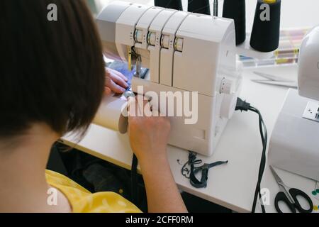 Par dessus, une femme brune non reconnaissable et coupée utilise une machine à coudre pour confecrer un vêtement en denim lors d'un atelier à domicile Banque D'Images