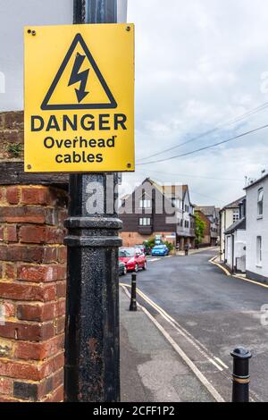 Avertissement jaune danger câbles plafonniers avertissement fixé à un poteau dans une route avec câblage électrique ci-dessus, en Angleterre, au Royaume-Uni. Banque D'Images