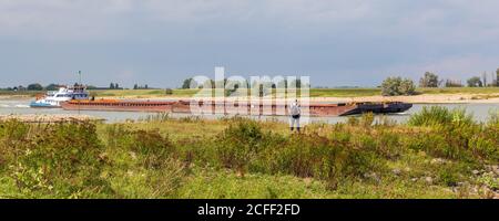 Homme regardant le pousseur bateau naviguant sur la rivière Waal près Nimègue aux pays-Bas Banque D'Images