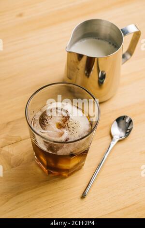 Du dessus de l'élégant verre avec du café noir glacé table en bois avec pichet à lait et cuillère Banque D'Images