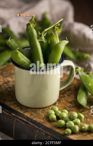 Pois frais et gousses de pois dans une tasse en émail un arrière-plan grunge Banque D'Images