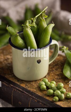 Pois frais et gousses de pois dans une tasse en émail un arrière-plan grunge Banque D'Images