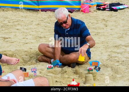Lyme Regis, Dorset, Royaume-Uni. 5 septembre 2020. Météo Royaume-Uni. Un grand-père faisant un château de sable sur la plage à la station balnéaire de Lyme Regis à Dorset sur une journée nuageux avec des sorts chauds et ensoleillés. Crédit photo : Graham Hunt/Alamy Live News Banque D'Images