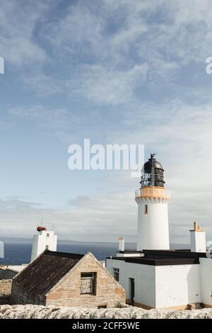 Magnifique phare blanc Dunnet Head dans les montagnes écossaises avec du bleu ciel et nuages blancs en arrière-plan Banque D'Images