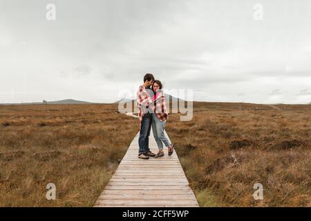 Couple de jeunes voyageurs couverts de écossais debout sur du bois Sentier parmi la tourbière brune en Écosse sur un ciel nuageux et sombre jour Banque D'Images