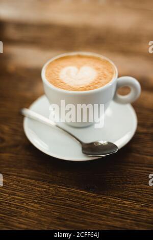 Tasse de cappuccino frais en forme de cœur sur mousse sur une table en bois dans le café Banque D'Images