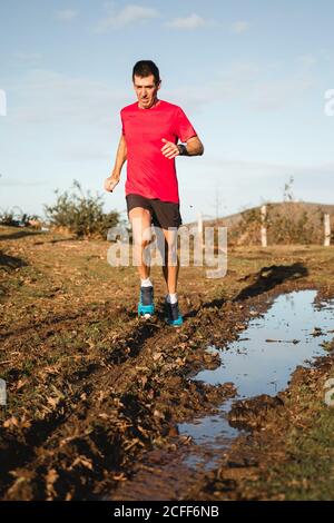 Par dessous de l'adulte en bonne santé actif homme en chemise rouge et short de jogging noir sur la route moyenne avec bas de porte jour d'automne ensoleillé avec ciel bleu ciel nuageux en arrière-plan Banque D'Images