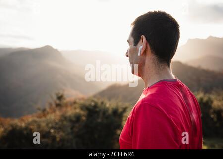 Vue latérale de l'homme sportif en chemises bleues et rouges en haut d'une colline verdoyante et en profitant du paysage détendez-vous après une course en montagne par beau temps Banque D'Images