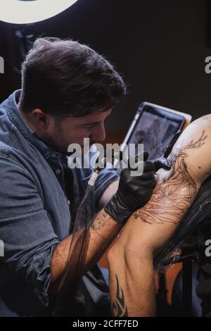 Maître faisant tatouage sur l'avant-bras du client mâle Banque D'Images