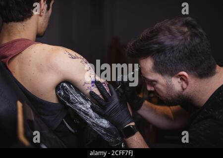 Maître faisant tatouage sur l'avant-bras du client mâle Banque D'Images