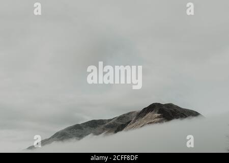 Sommets isolés entourés de nuages sous ciel gris en brouillard jour Banque D'Images