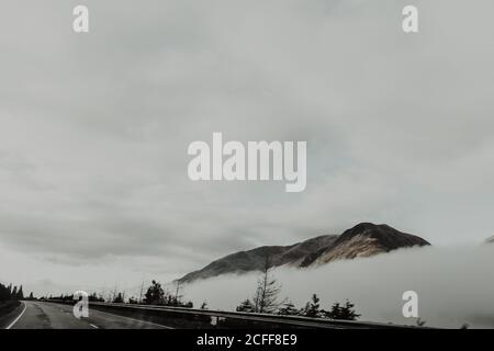 Sommets isolés entourés de nuages sous ciel gris en brouillard jour Banque D'Images