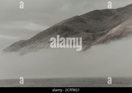 Sommets isolés entourés de nuages sous ciel gris en brouillard jour Banque D'Images