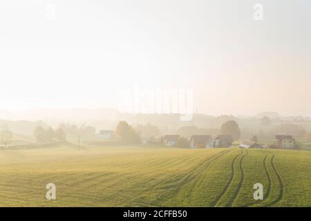 Vue sur le paysage d'un vaste champ avec des sillons situés près du village maisons sous la colline à la lumière du jour dans la campagne avec brouillard loin loin Banque D'Images