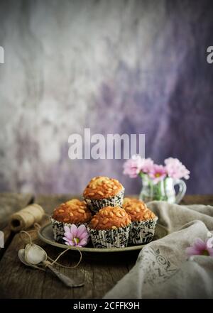 Assiette avec muffins savoureux de grain placé près de la serviette de lin et fleurs roses sur une table en bois Banque D'Images