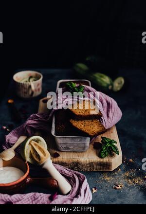 De dessus savoureux gâteau au chocolat garni de pétales de fleur et basilic et placé sur la table avec des courgettes vertes et aigre crème dans un bol Banque D'Images