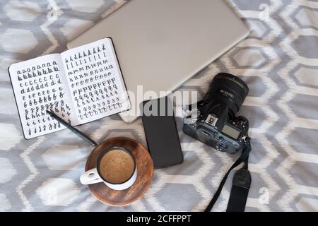 Vue de dessus du bloc-notes ouvert et d'une tasse de café chaud composé d'un appareil photo et d'un ordinateur portable sur un lit confortable Banque D'Images