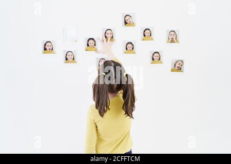 Jolie petite fille dans une robe jaune est debout sur son dos plaçant des photos d'elle-même montrant diverses émotions Banque D'Images