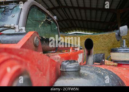 Cabine et tuyau d'échappement du tracteur rouge en bure garage sur la cour de ferme près des piles de foin Banque D'Images