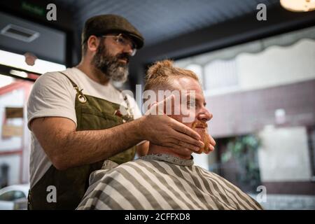 Coiffeur effectuant un massage du visage à un beau redhead homme avec assis sur la chaise Banque D'Images