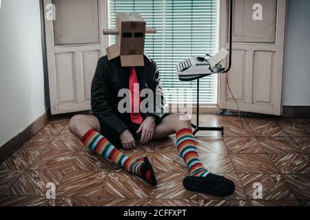 Vue latérale de l'auteur masculin portant une boîte en carton et dénudée chaussettes debout près de la table avec machine à écrire rétro et regardant vers le bas Banque D'Images