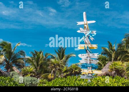 Poteau en bois avec panneau coloré montrant les directions vers les pays du monde Dans les palmiers verts de la côte du Mexique Banque D'Images