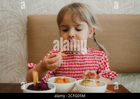 Petite fille mignonne mangeant des en-cas appétissants variés à table Banque D'Images