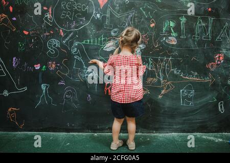 Vue arrière de dessin d'enfant adorable et méconnaissable à l'école pendant classe dans un tableau vert d'écriture Banque D'Images