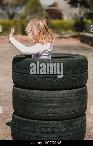 De derrière anonyme de petite fille debout dans la pile de pneus de voiture tout en s'amusant et en jouant à l'extérieur l'été jour Banque D'Images