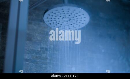 Design contemporain avec pomme de douche ronde en chrome et eau courante dans la salle de bains Banque D'Images